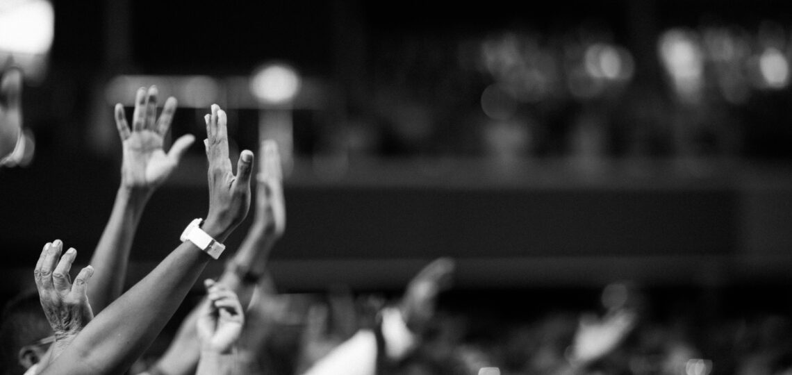 Black and white image of audience with hands raised, capturing concert energy.